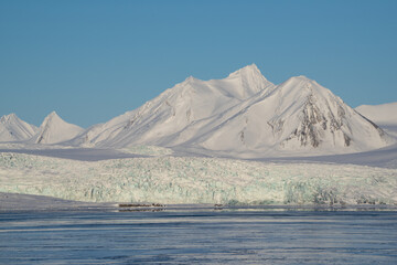 Glacier front on Spitsbergen during spring with blue sky and snow covered mountains.