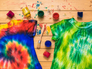 Two tie dye t-shirts and a fabric painting kit on a wooden table. Flat lay.