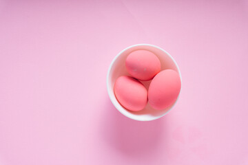 Three pink eggs inside the white bowl over pink background.