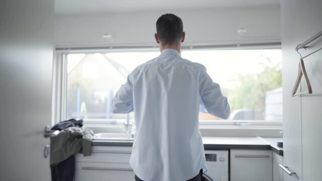 MS ZI Man putting on white shirt in laundry room / Denmark
