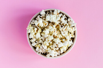 Popcorn in a pink bowl on pink background, top view close-up