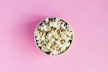 Popcorn in a pink bowl on pink background, top view