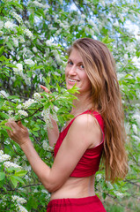 A young blonde woman with long hair in a red dress next to white cherry blossoms. Aromatherapy, anti-stress concept.