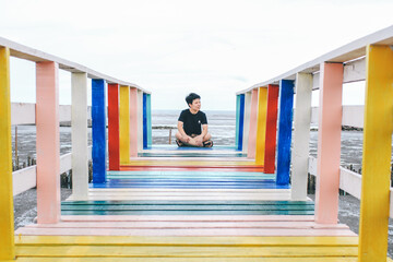 Alone traveler relax siting on colorful rainbow wooden bridge extends into the mangrove sea tourist attractions in Thailand,Active lifestyle concept.Lonely travel because of the corona virus