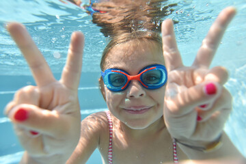 Portrait of cute girl with goggles swimming under pool water