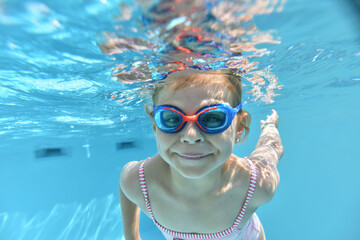 Portrait of cute girl with goggles swimming under pool water