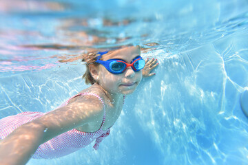 Naklejka premium Portrait of cute girl with goggles swimming under pool water