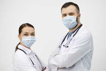 Two male and female doctors in white lab coat and protective masks standing opposite each other and looks at camera on white background. Healthcare support, medical workers, pandemic virus infection