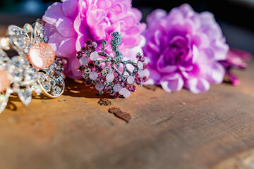 A composition of women's jewelry and accessories in pink on an old wooden surface. Brooch with colored stones, hairpins and flowers in delicate shades