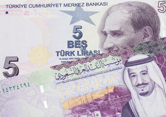 A close up image of a purple five Turkish lira bank note with a five Saudi riyal bill in macro from Saudi Arabia