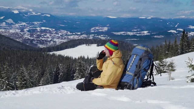 Traveller in the mountains in winter. Hiker sits in the snow and talks on the phone. Winter sports and recreation hiking concept. Carpathian mountain range. 4K