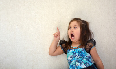 I know answer! Little girl in a beautiful outfit holds the index finger up with an open mouth and the emotion Wow and surprised face. The human emotions, facial expression concept, copy space. 