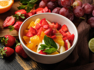 Dessert salad with ice cream and summer fruits mix in bowl on table background with ingredients