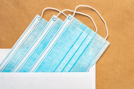 Blue medical surgical face masks in white postal envelope on yellow craft paper background. Flat lay, close-up view. Concept caring for loved people at distance, forced during pandemic social distance