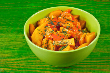 Potatoes with parsley in a green bowl on a wooden table. Boiled potatoes with orange sauce. Food in utensils on the background of an old pink board.