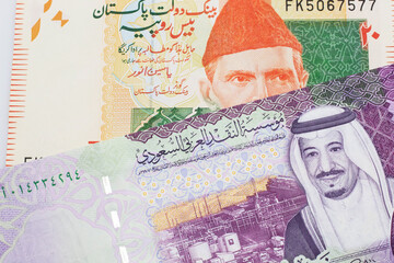 An orange and green twenty Pakistani rupee bank note with a five Saudi riyal bank note in macro