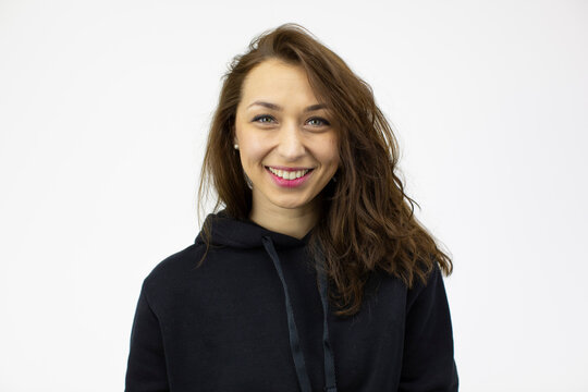 Portrait of young beautiful smiling woman with long dark curly hair wearing black hoodie looking at camera isolated on white background. Happy positive girl in casual wear, copy space