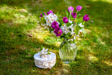 Bouquet of purple tulips and pink apple flowers in glass vase on the lawn background. Holiday background, copy space. Mothers day, birthday concept.