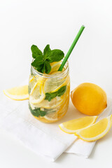 Lemonade in a glass jar with green paper straw, lemon slices and mint on the white napkin. Closeup. 