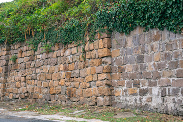An old wall made of regular-shaped stone blocks covered with green vegetation