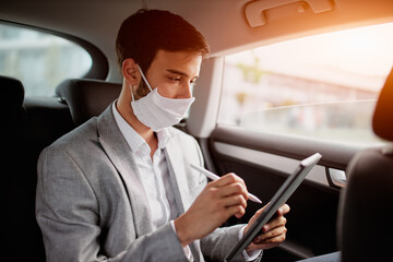 Young man wearing a face mask sitting in the car and using digital tablet