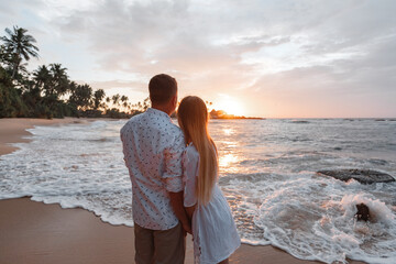 Young woman traveler holding man's hand and looking beautiful sunset on the beach, Couple on vacation in summer concept