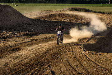 Motocross rider on dirt track creates a cloud of dust and debris. Extreme sport activity. Late summer day