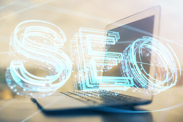 Double exposure of table with computer and seo drawing hologram. Search optimization concept.