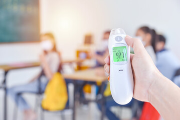 Digital thermometer, thermometer gun on teacher hand using for check body temperature of students before going into classroom for study.