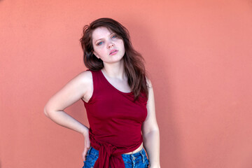 Sensual expression - Girl half-length portrait on a pink background. Brunette girl in casual clothes, sleeveless red t-shirt and denim shorts. Half-length portrait on a colored background, the facial 