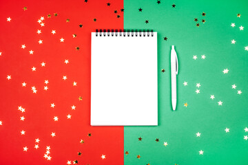 White notebook and pen on a red-green background with golden stars. Plans for the new year. 2021 celebration