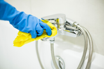 A woman wearing gloves cleaning a bathtub