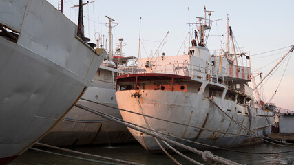 Naklejka premium Side view of the old metal ships moored at shipyard during awaiting for repair and maintenance in evening time