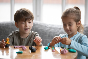 Obraz premium Little preschooler boy and girl children engaged in creative activity with playdough at home, small brother and sister play with modeling clay Play-Doh, do figures together, craft, hobby concept
