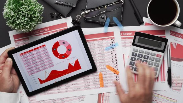 Top view of businessman's hands working with tablet pc and financial reports. Modern black office desk with notebook, pencil and a lot of things. Flat lay table layout.
