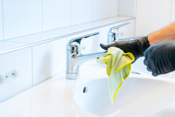 professional cleaner polishes a bathroom sink and faucet with a yellow micro fiber cloth