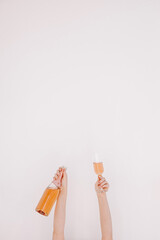 Female hands hold bottle of rose champagne and glass against white wall. Happy Birthday, anniversary party holiday celebrating decoration festive concept