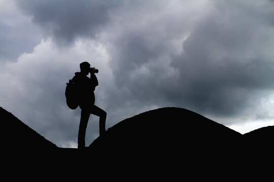 Silhouette of a man with backpack in the mountains is taking pictures of the landscape