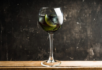 Black cocktail with lime slices in wine glass on the rustic background. Selective focus. Shallow depth of field. 