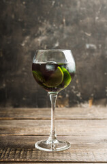 Black cocktail with lime slices in wine glass on the rustic background. Selective focus. Shallow depth of field. 