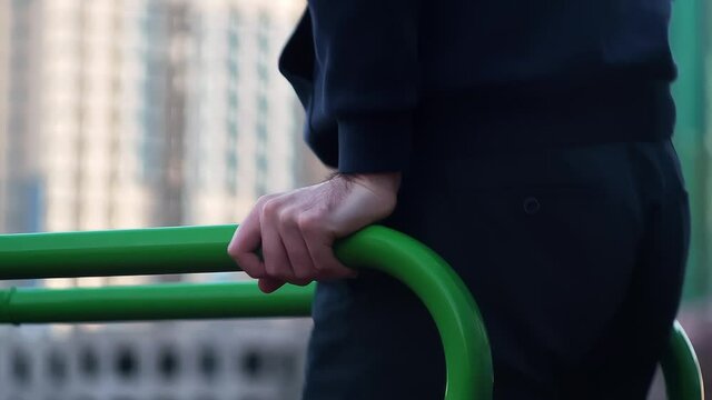 Young man doing dips on parallel bars outdoors with sunrise city on the back