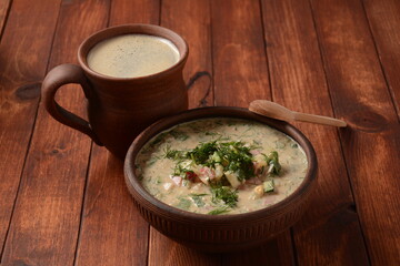 Russian cuisine- Okroshka, Summer light cold yogurt soup with cucumber, radish, eggs and dill with sour cream  and green onion on a  wooden table.  