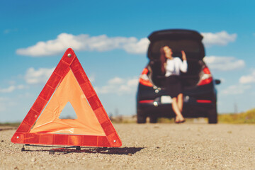 Nice business woman talking on the smartphone while warning triangle is .on the road. Broken car. Accident with an auto. Toned