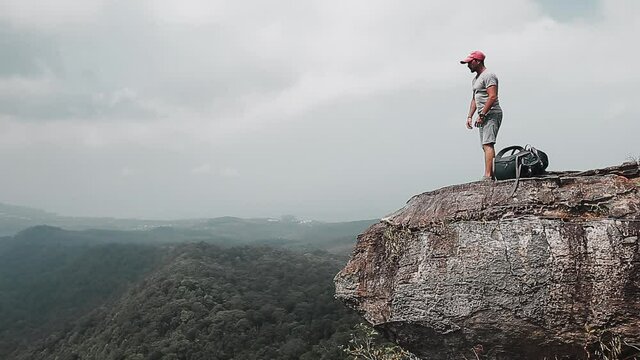 Backpacker with valley view. Hiker man comes to the edge of the mountain and then lied down to the ground with backpack using as a pillow