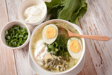 Green sorrel and spinach soup with boiled egg, spring onion and sour cream on white wooden rustic...