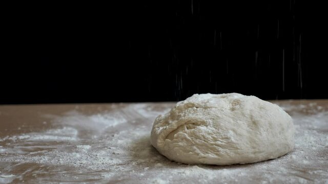 Raw bread is prepared for baking on a black background on the table. The bread is sprinkled with flour to make it crispy. This video was taken close-up with natural light in 4k