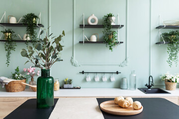 A vase with green plant on a table. Scandinavian classic kitchen with wooden and vintage details, minimalistic interior design. Real photo.Cosy home. 
