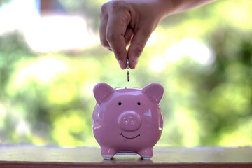 Close-up shot of a woman putting a coin in a piggy bank. Money saving concept.