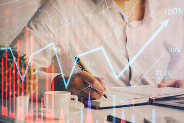 Double exposure of man's hands writing notes of stock market with forex chart.