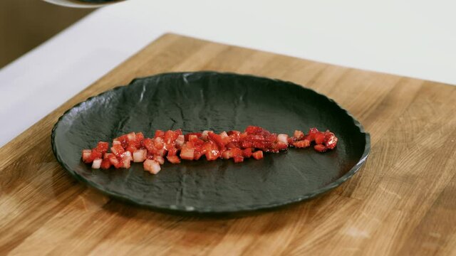 Cooking of strawberry dessert. Close-up of chef putting chopped strawberries onto the plate with tablespoon. 4K